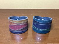 Two vintage handmade leather bracelets with multicolored leather strips placed side by side on a wooden surface.