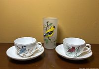 Front view of the two bird cups and saucers with the Goldfinch water glass centered behind them.