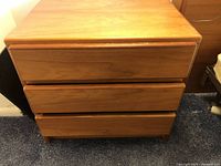 Front view of one nightstand showing three drawers with integrated horizontal wooden handles and light brown wood finish.