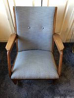 Front view of blue upholstered rocker showing button tufted backrest and wooden armrests.