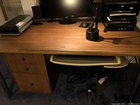 Full view of wooden computer desk with computer monitor, lamp, and keyboard tray pulled out beneath the surface. Three drawers on left side visible.