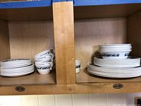 Corelle Old Town Blue dinnerware stacked on wooden shelves, showing plates and cups arranged.