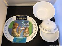 Set of Corelle Snowflake Blue ceramic bowls and platters arranged on a dark surface, showing their size and pattern.