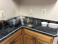 Multiple glass and ceramic bowls and baking dishes arranged on kitchen countertop, various sizes and colors, clear and brown glass, white ceramic pieces