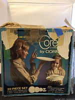 Box of Corning Snowflake Blue 20-piece dinnerware set showing wear but intact with vintage graphics featuring a woman and child.