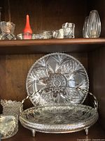 Shelf with a large cut glass round platter with handles and feet, crystal bowl, candleholders, and glass coasters