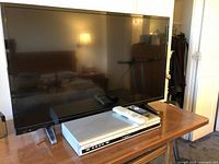 Insignia 39-inch TV on wooden table with Toshiba DVD player and two remotes on top, showing front of TV and DVD player