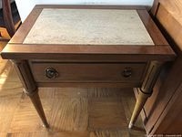 Wooden end table with beige stone inlay top, single drawer with metal ring handles, and tapered legs with wear visible
