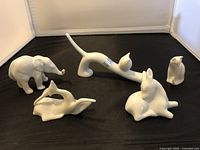 All five figurines arranged on black background: elephant, dolphin, stretching cat, sitting bunny, and penguin.