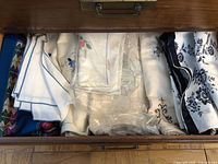 Drawer containing folded embroidered tablecloths and napkins with varied colors and patterns.
