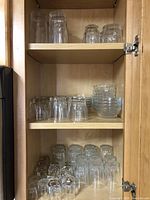 Multiple clear drinking glasses and bowls arranged on wooden shelves inside a cabinet