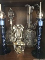 Three crystal decanters with stoppers and two blue glass candlesticks shown on a shelf, highlighting intricate cut glass designs and colored glass details.