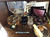 Display of assorted Judaic items including fabric challah covers, knit yarmulke, candle holders, dreidel, and tzedakah boxes on a shelf.