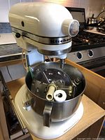 KitchenAid white stand mixer with stainless steel bowl and attachments inside. Shows wear on the outside.