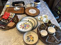Overview of assorted kitchenware on table including plates, trays, corkscrews, pots, and small accessories.