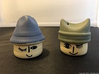 Front view of two ceramic salt and pepper shakers shaped with faces and hats, one with a blue hat and the other with a green hat.
