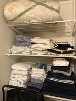 Shelves of folded sheets, pillowcases, towels and black laundry cart