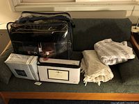 Wide view of couch showing comforter in black packaging, several folded linens including tablecloths, and sheet sets in plastic packaging