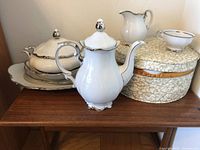 Group view of coffee pot, covered dish, pitcher, served on console