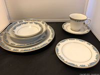 Photo displaying various plates and teacup with saucer, featuring blue and gold rim design on fine china