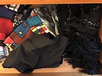 Scarves with solid black, colorful geometric patterns, and shiny black scarf in drawer