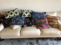 Photo of 10 assorted throw pillows in various colors and patterns on a cream-colored sofa.