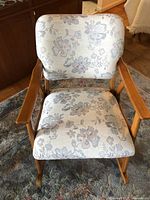 Front view of wooden rocking chair with floral patterned fabric upholstery on seat and backrest, showing overall condition and design.