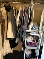 Closet rack with mixed women's clothing items including dresses, blouses, and folded garments in baskets