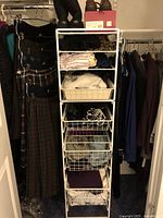 Closet view showing hanging skirts and coats on left and right, wire basket shelves in center with folded sweaters and tops.