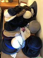 A collection of various women's vintage hats piled on a table, showing multiple styles and colors, including fur, wool, crochet, and decorative hats.