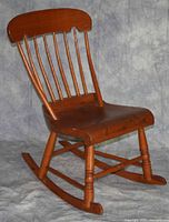 Full view of wooden rocking chair with rounded spindle back and visible cracks on seat surface.
