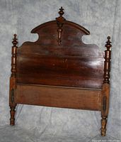 Dark wood bed frame headboard and footboard with turned spindles and carved crest visible.