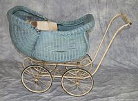 Side view of a blue wicker doll carriage showing metal frame and wheels. Bonnet curved and closed.