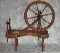 Side angle of antique wooden bobbin winder showing wheel and overall structure