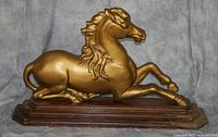 Front view of gold-painted cast iron horse statue on layered wooden base