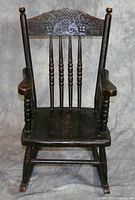 Black wooden children's rocking chair with floral decorations on the top back rail, showing significant varnish chipping.