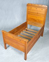 Child's wooden bed frame with decorative carved floral motifs on headboard and footboard, showing overall frame shape and partial slats inside.