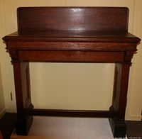 Front view of the tall oak clerk's desk showing its dark brown varnish and panelled legs with a raised backboard.