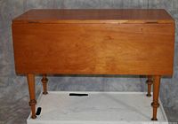 Photo of the table with both drop leaves down, showing rectangular top with light brown varnish and turned legs.