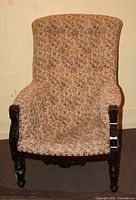 Front view of floral upholstered easy chair showing patterned beige fabric and carved dark wood armrests and legs.