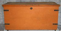 Large orange blanket chest with flat top and visible metal hinges, some scratches and scuffs.