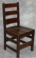 First wooden desk chair showing ladder back design with three slats and visible wear on seat and wood edges.