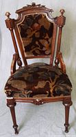 Frontal photo of one carved wooden dining chair showing floral upholstery and intricate wood detailing on legs and backrest.