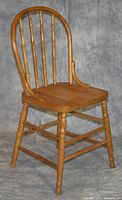 Front-side view of one wooden dining chair showing arched backrest with turned spindles, turned legs and stretchers, contoured wooden seat, worn finish.