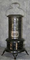Front view of the full oil stove showing cylindrical shape, perforated top section with handle, and three curved legs.