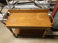 Full view of the pine washstand showing top surface with two vertical side rails and the bottom shelf, with turned legs.