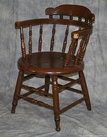 Full view of round back wooden chair with spindle details showing worn brown finish and some chipping on armrest.
