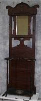 Front view of Victorian wooden upright hall stand with mirror attached, umbrella holders, and coat hooks, showing wear and wood detail.
