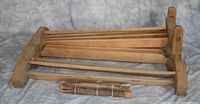 Wooden flax breaker with frame and bundled wooden rods shown from side angle on fabric surface.
