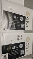 Pair of certified moissanite stud earrings alongside GRA certification cards showing diamond-quality attributes and warranty information.